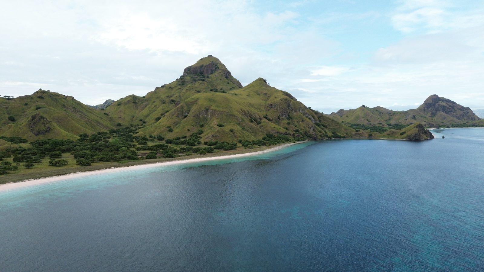 Padar – Aerial jagged green ridge, curved white beach (Real photo from a Komodo Explorer trip)
